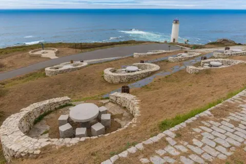 Faros de la Costa da Morte vigilando el Atlántico. Bancos de piedra y mesas invitan a contemplar el paisaje marino.