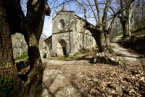 Antiguo monasterio Santa Cristina, rodeado de árboles desnudos y hojas secas. Un camino serpentea hacia la entrada principal.