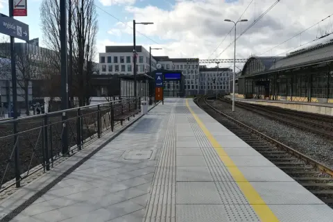 Peron 6 na dworcu Wrocław Główny, z którego odjeżdża pociąg. Nowoczesny peron z żółtym pasem bezpieczeństwa i budynkami w tle.