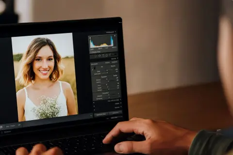 Un portrait de femme souriante est retouché sur un ordinateur portable. Lightroom sert à améliorer la luminosité, les couleurs et les détails pour un rendu parfait.