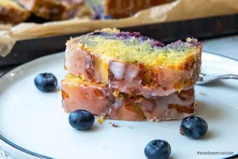 Zwei Scheiben saftiger zitronen blaubeer kuchen mit Zuckerguss und frischen Blaubeeren auf einem Teller.