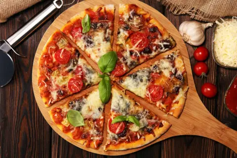 Pyszna pizza z pomidorkami i bazylią, obficie posypana serem do pizzy. Obok czosnek, pomidorki i sos.