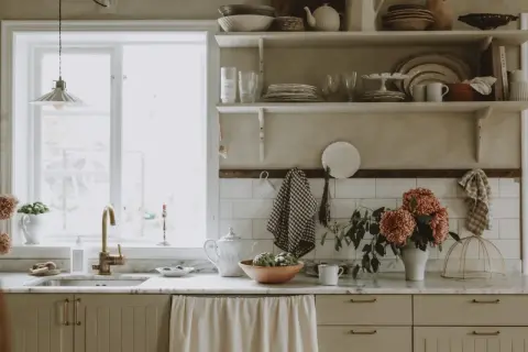 Köksbänk med diskho, kran och blommor. Skåpluckor i ljusbeige färg, redo att måla luckor för en ny stil.