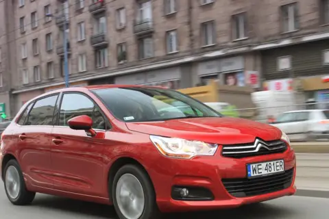 Czerwony Citroen C4 1.6 HDI w ruchu miejskim, z budynkami w tle.