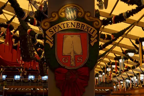 Spatenbräu-Schild mit Schaufel-Symbol, das auf die Herkunft des Bieres hinweist. Festlich geschmückte Halle.