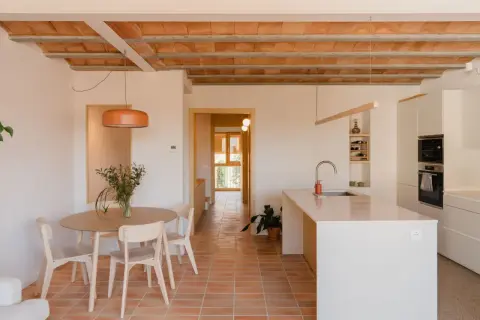 Interior de una vivienda antigua renovada, con suelo de terracota, vigas de madera a la vista y cocina moderna.