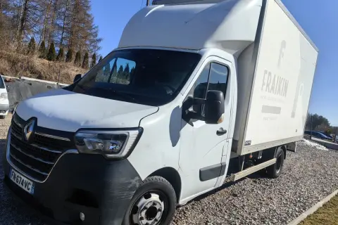 Biały bus z zabudową typu bliźniak, zaparkowany na żwirowym podjeździe.