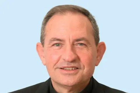 Retrato de un hombre mayor con sotana negra, sonriendo. Podría ser el párroco de San Pedro de Osma.