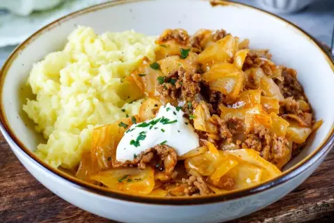 Herzhaftes Schmorkohl mit Hackfleisch, garniert mit einem Klecks Sour Cream und Petersilie, serviert mit cremigem Kartoffelpüree.