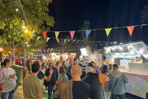 Noche animada en un festival de ebro food trucks, con luces, banderas y gente disfrutando.