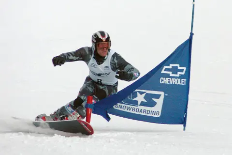 Snowboardzista w kasku i goglach mija niebieską flagę z logo Chevrolet. To sport, który zyskał popularność w XX wieku, choć jego korzenie sięgają wcześniejszych lat.