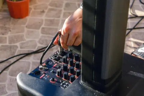 Ręka podłącza kabel do miksera, pokazując, jak podłączyć przedwzmacniacz do wzmacniacza.