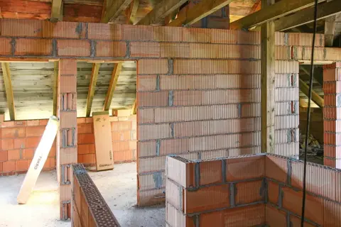 Budowa domu w toku: wznoszone są ściany z pustaków ceramicznych, widoczna ścianka kolankowa i drewniany strop.