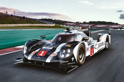 Porsche 919 Hybrid pędzi po torze wyścigowym, oznaczony numerem 1, w barwach czarno-białych z flagą Niemiec.