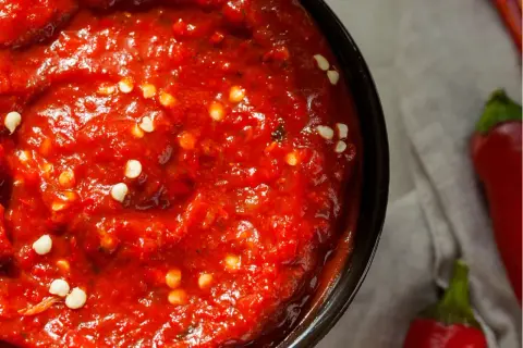 Nahaufnahme einer Schüssel mit leuchtend roter Harissa-Paste, gesprenkelt mit weißen Chiliflocken. Ein einfaches harissa rezept.