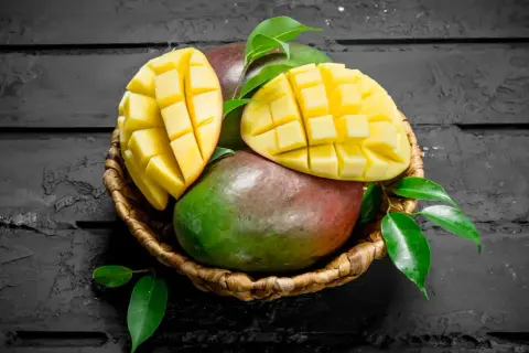 Koszyk z dojrzałymi mango, jedno przekrojone na pół, ukazujące soczysty miąższ. Interesuje Cię mango indeks glikemiczny?