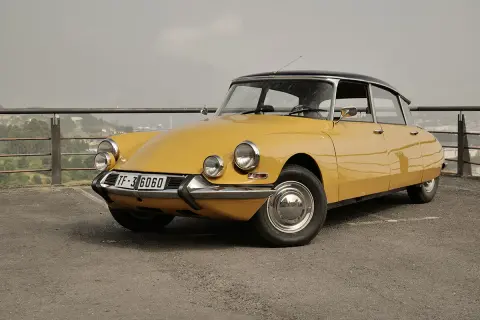 Citroën Tiburón amarillo, un clásico icónico con su diseño aerodinámico y faros distintivos, aparcado en un mirador con vistas a la ciudad.