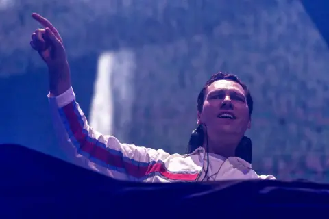 DJ Tiësto wznosi rękę, wskazując na tłum podczas jednego ze swoich energetycznych koncertów.