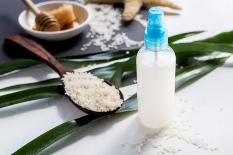 Bouteille de spray remplie d'eau de riz, avec une cuillère de riz et du miel en arrière-plan.