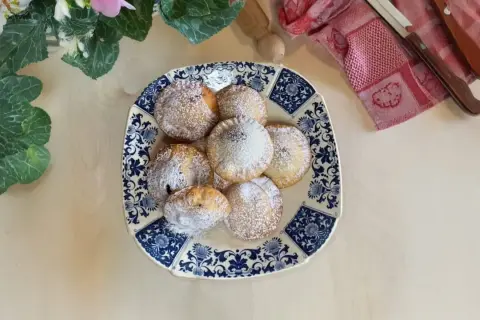 Piatto di ravioli al cioccolato spolverati di zucchero a velo, decorato con fiori e foglie verdi.