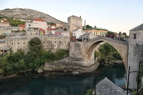 Stari Most, en ikonisk stenbro i Mostar, sträcker sig över en turkos flod. Gamla stenbyggnader och en moské omger den.