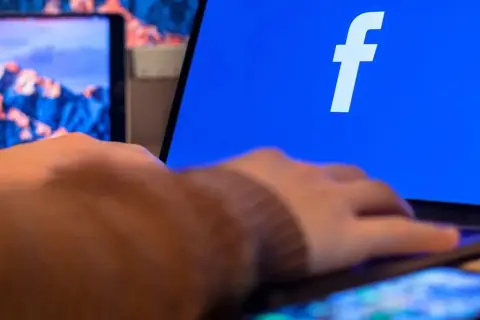 Dłoń na klawiaturze laptopa, na ekranie logo Facebooka. Dowiedz się, jak utworzyć stronę na Facebooku.