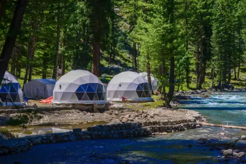 Dome-shaped namioty w lesie nad rzeką to przykład, co to jest glamping. Luksusowy wypoczynek na łonie natury.