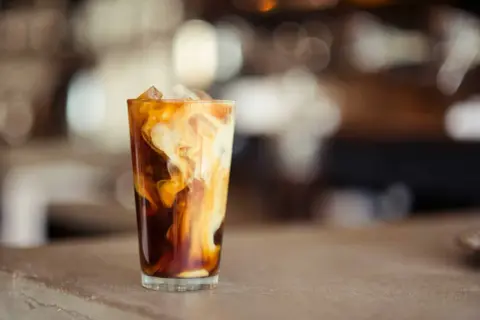 Un verre de latte glacé avec des tourbillons de crème dans le café sombre, sur un comptoir.