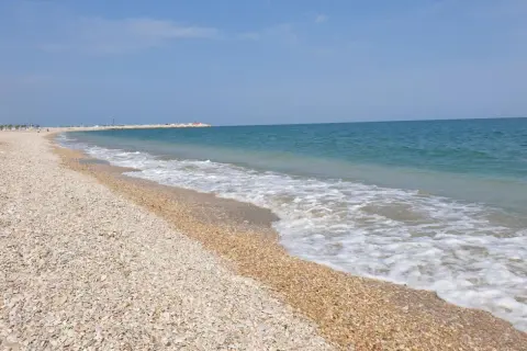 Spiaggia di ciottoli a Civitanova Marche, con il mare azzurro e le onde che lambiscono la riva.