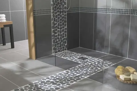 Douche italienne moderne avec carrelage imitation pierre de galets sur le sol et les murs. Un banc en bois et des serviettes ajoutent une touche chaleureuse.