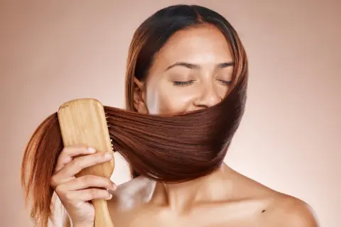 Frauen mit geschlossenen Augen bürsten ihr glänzendes, braunes Haar mit einer Holzbürste. Ein Moment der Ruhe und des **Haare pflegen**.