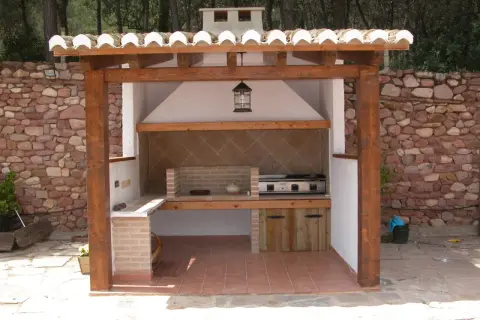 Barbacoa de obra con estructura de madera y tejado de tejas. Ideal para aprender como hacer una barbacoa de obra y disfrutar del exterior.