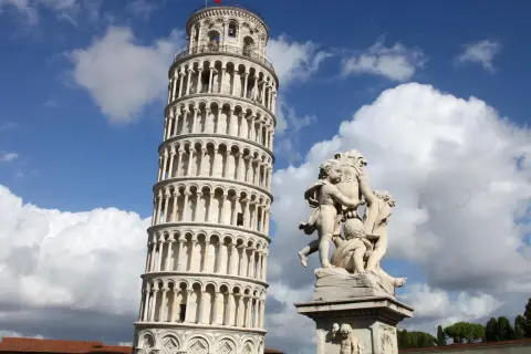 La Torre Pendente di Pisa, con la sua inconfondibile inclinazione, si erge maestosa sotto un cielo azzurro e nuvoloso, accanto a una scultura di putti.
