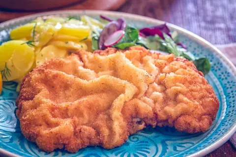 Ein knuspriges Schnitzel Wiener Art mit goldbrauner Panade, serviert mit Kartoffelsalat und frischem Grün.