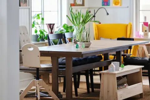 Un banco almacenaje de madera clara, perfecto para guardar libros y objetos, complementa la mesa de comedor.