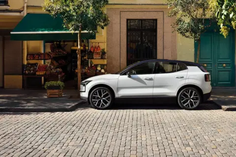 Vit Volvo parkerad på kullerstensgata framför en färggrann fasad. Upptäck olika volvo utrustningsnivåer för din nästa bil.