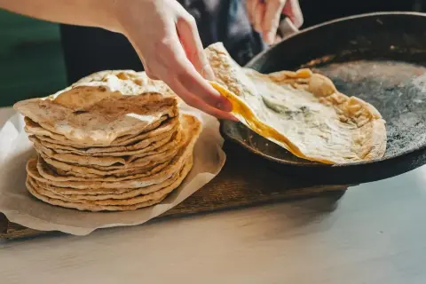 Stos świeżo upieczonego lawaszu obok patelni, na której właśnie smaży się kolejny. Pyszne, cienkie placki gotowe do podania.