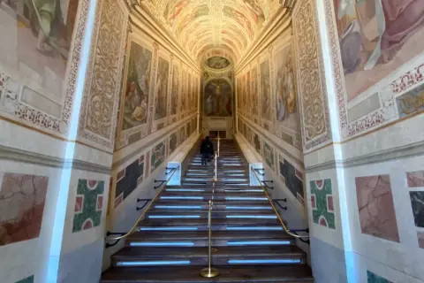 Persona subiendo la escalera santa de Roma, con frescos en las paredes y una crucifixión al final.