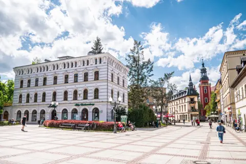 Słoneczny dzień na placu w parku zdrojowym w Cieplicach Śląskich-Zdroju. Ludzie odpoczywają na ławkach, spacerują.