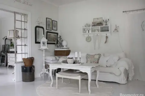 Ett rum med shabby chic inredning. En vit soffa med kuddar, ett vitt bord med ljus och en rund matta.