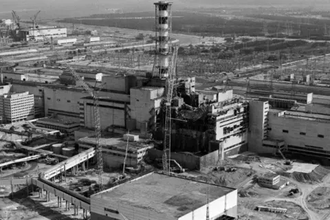 Widok zniszczonego reaktora w Czarnobylu, symbol tragedii i **czarnobyl ofiary**. W tle widać inne budynki elektrowni i żurawie.