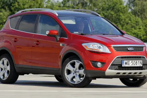 Czerwony Ford Kuga na parkingu. Kierowca w środku. Wiele osób szuka ford kuga opinie przed zakupem.