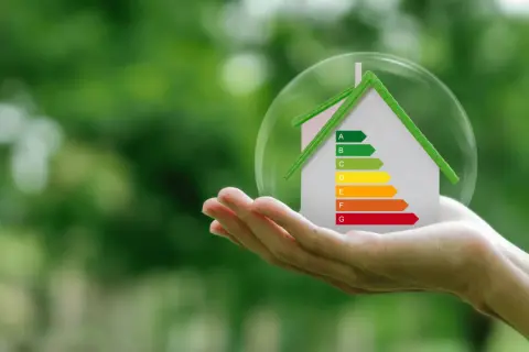 Mano sostiene casa con etiqueta energética, simbolizando la deducción IRPF por eficiencia energética.