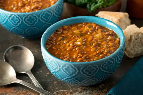 Bol de soupe de lentilles savoureuse, une recette réconfortante avec du pain et des couverts.