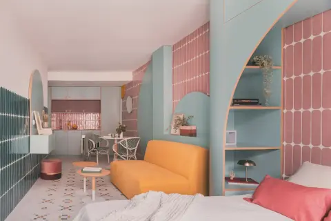 Habitación de 4 metros cuadrados con sofá amarillo, estanterías turquesas y detalles en rosa. Cocina y comedor integrados.