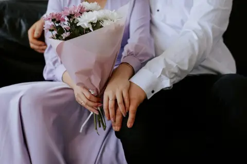 Un couple se tient la main, un bouquet de fleurs roses et blanches à la main. Un rappel doux de leur calendrier noces.
