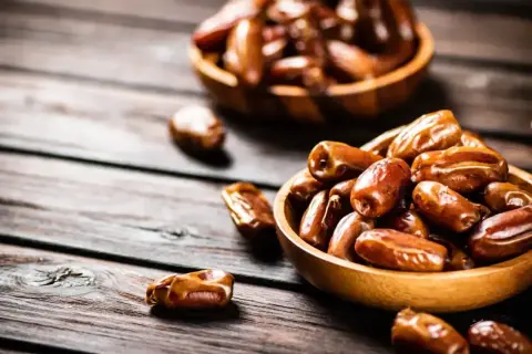 Dwa drewniane miseczki pełne daktyli. Te słodkie owoce, choć bogate w daktyle kcal, są pyszną i energetyczną przekąską.
