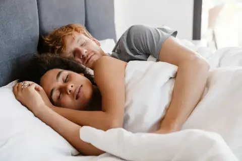A couple sleeps peacefully, their bodies intertwined. Do you sleep better next to someone you love?