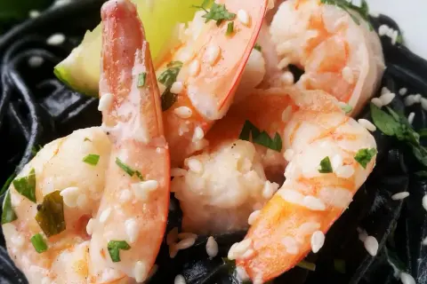 Krewetki na czarnym makaronie, posypane sezamem i ziołami, z kawałkiem limonki.