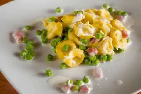 Tortellini di carne con piselli e pancetta, un classico condimento per un primo piatto gustoso e cremoso.